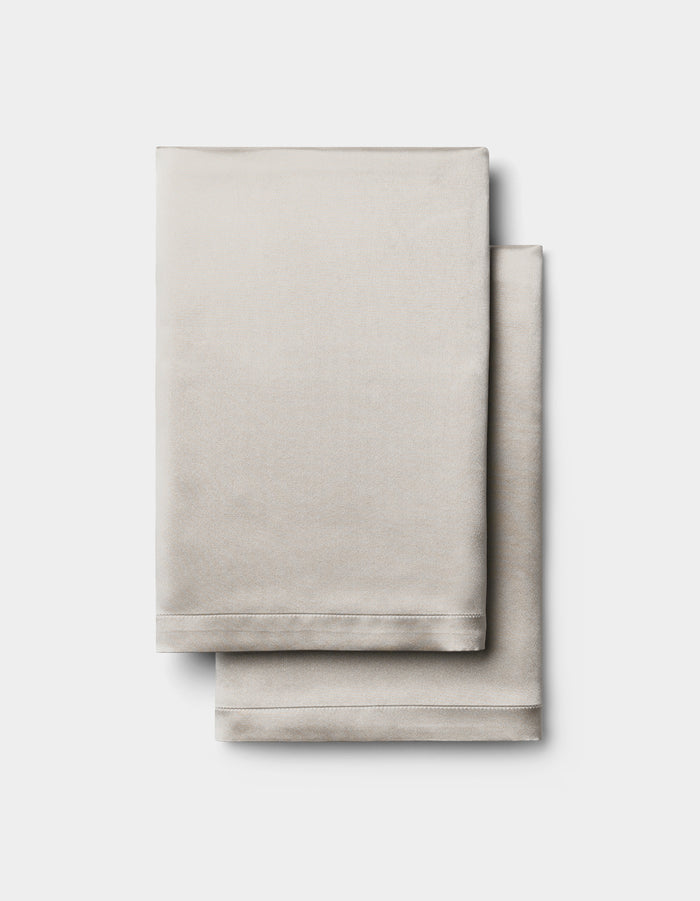 Two neatly folded Cozy Earth Silk Pillowcases in light beige are stacked together against a plain white background.|Color:Dove Grey
