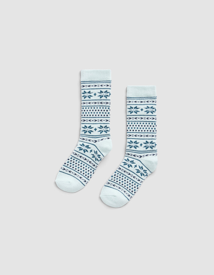 The Cozy Earth Snowflake Plush Lounge Sock features light blue fabric with dark blue geometric and snowflake stripes, shown on a plain light gray background.|Color:Mist
