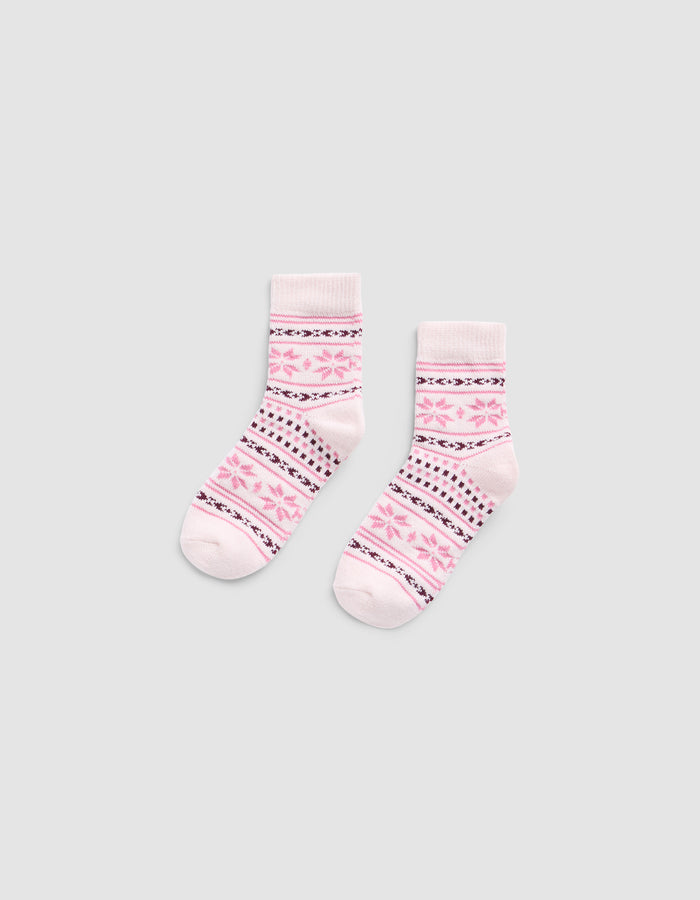 The Snowflake Plush Modern Crew Sock by Cozy Earth is a light pink pair featuring darker pink and black geometric patterns, including stripes and star shapes, displayed flat on a plain gray background.|Color:Ballet