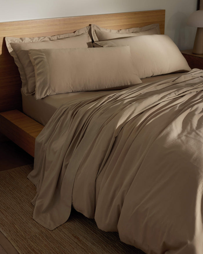 A neatly made bed features Cozy Earth's Soft-Wash Cotton Pillowcases in light brown, with matching sheets and comforter on a wooden frame. The bedding feels smooth and soft, complementing the room's minimal, warm-toned decor.|Color:Sandalwood