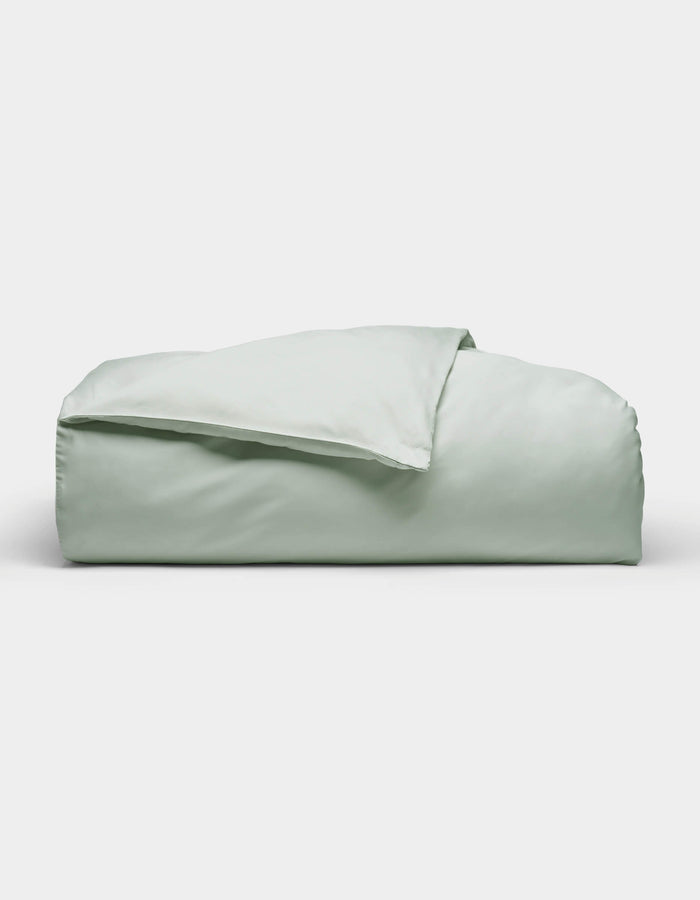 The Soft-Wash Cotton Duvet Cover by Cozy Earth, shown neatly folded in light green, is displayed against a plain white background.|Color:Laurel