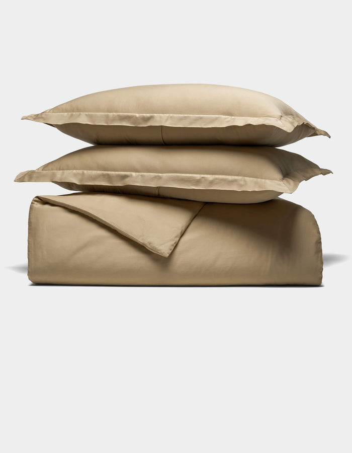 The Cozy Earth Soft-Wash Cotton Duvet Set, featuring two stacked pillows, a folded sheet, and a folded duvet cover in beige, is neatly arranged against a plain white background.|Color:Sandalwood