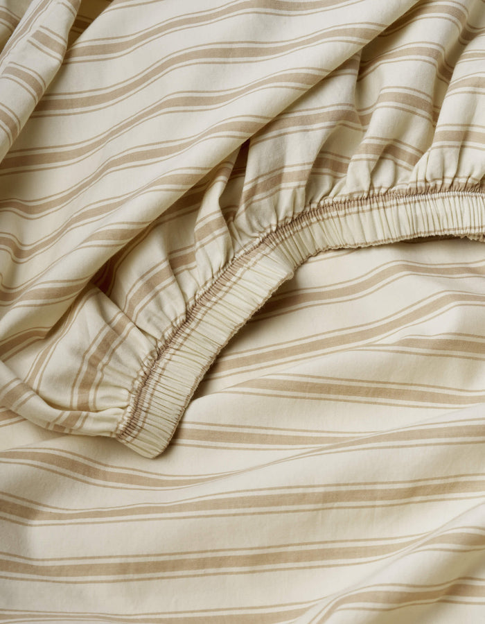 The Soft-Wash Cotton Fitted Sheet by Cozy Earth features a beige color with light brown horizontal stripes and an elastic edge, showcasing its gathered fabric detail, texture, and pattern.|Color:Coconut and Sandalwood Stripe