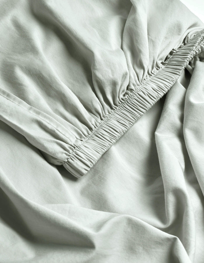 Close-up of Cozy Earth's Soft-Wash Cotton Fitted Sheet in light gray, featuring ruched elastic edges that create gentle folds and a textured, smooth, and lightweight surface.|Color:Laurel