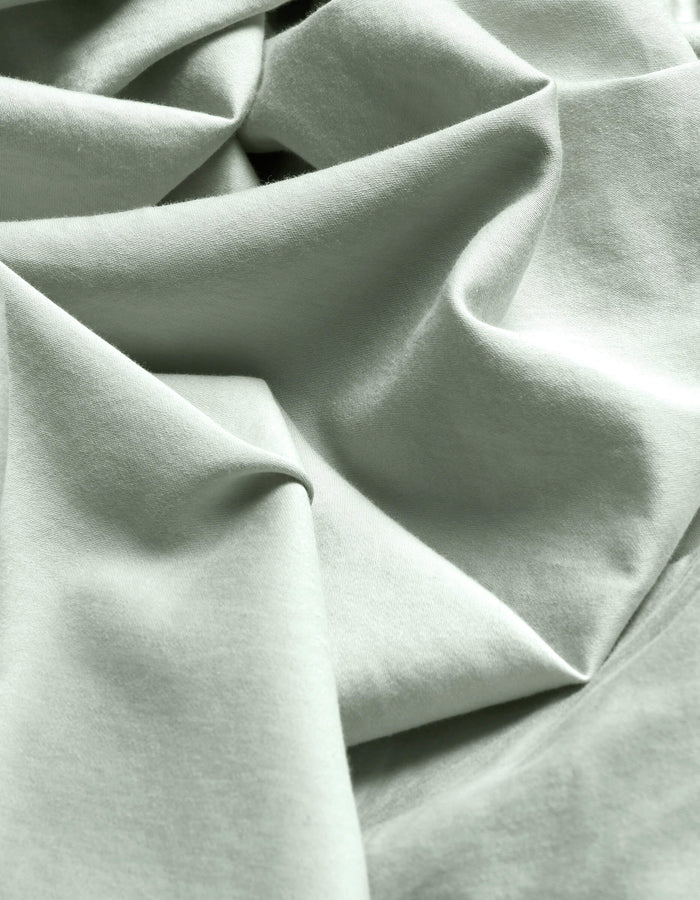 Close-up of Cozy Earth's Soft-Wash Cotton Flat Sheet in light mint green, featuring soft folds, gentle wrinkles, a subtle weave, and delicate shadows.|Color:Laurel