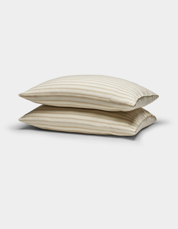 Two Cozy Earth Soft-Wash Cotton Pillowcases in beige with thin horizontal brown stripes are stacked against a plain white background.|Color:Coconut and Sandalwood Stripe