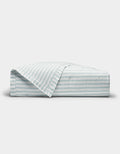 The Cozy Earth Soft-Wash Cotton Quilt is shown neatly folded with one corner turned back, revealing its light color and thin horizontal blue and gray stripes against a plain white background.|Color:River and Sea Salt Stripe