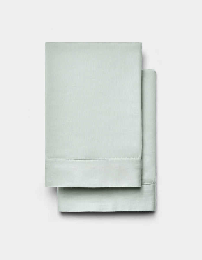 A pair of Cozy Earth Soft-Wash Cotton Shams in light green is neatly folded and displayed against a plain white background.|Color:Laurel