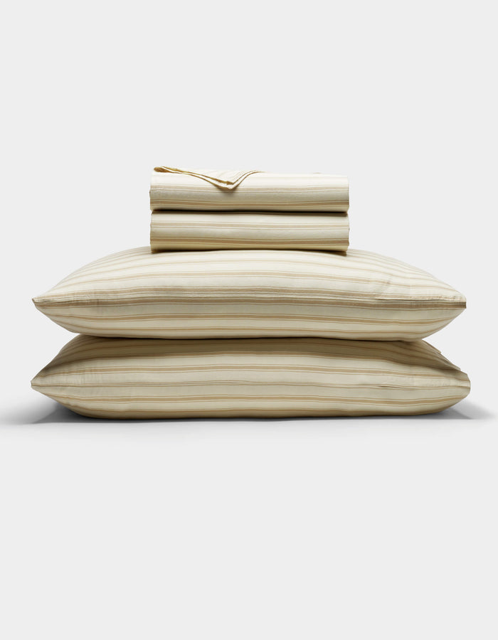 The Cozy Earth Soft-Wash Cotton Sheet Set in beige and light brown stripes is neatly stacked with two pillows at the base, topped with folded sheets and a pillowcase, displayed against a plain white background.|Color:Coconut and Sandalwood Stripe