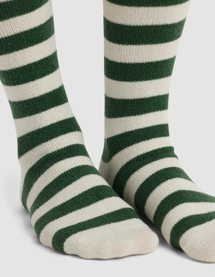 Close-up of feet wearing Cozy Earth's The Striped Plush Lounge Sock, featuring thick, horizontal dark green stripes on white, standing on a white background.|Color:Celadon Stripe
