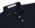 The Anderson Shirt: Black, featuring a dark-navy polo with a classic point collar, three white buttons, and a woven label, offering stretch and moisture-wicking comfort.