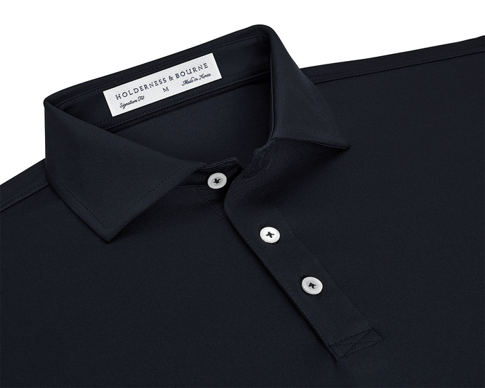 The Anderson Shirt: Black, featuring a dark-navy polo with a classic point collar, three white buttons, and a woven label, offering stretch and moisture-wicking comfort.