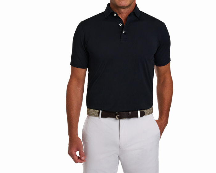 Man wearing The Anderson Shirt: Black, a short-sleeve polo with a structured collar, tucked into light trousers, featuring a braided belt and relaxed posture.