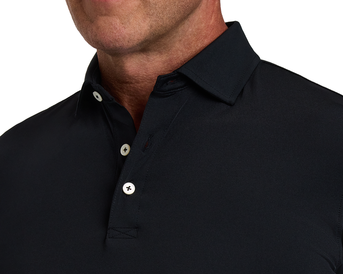 Close-up of a person wearing The Anderson Shirt: Black, highlighting its structured spread collar, partially buttoned placket, and jersey knit performance fabric for comfort and style.