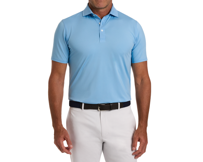 Man wearing The Anderson Shirt: Vista Blue, a light blue polo with a structured collar, tucked into off-white trousers with a dark braided belt.