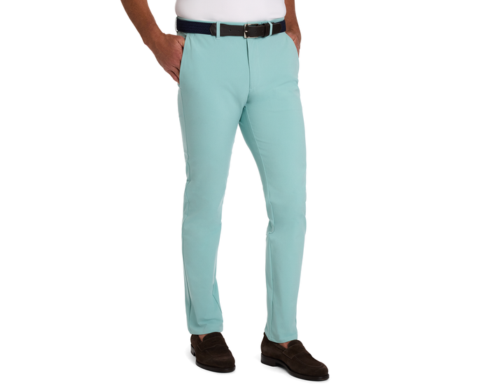 Model wearing The Anson Chino Pant: Cascade Green with slant pockets, navy belt, and dark brown loafers, showcasing wrinkle-resistant, quick-dry, stretch fabric.
