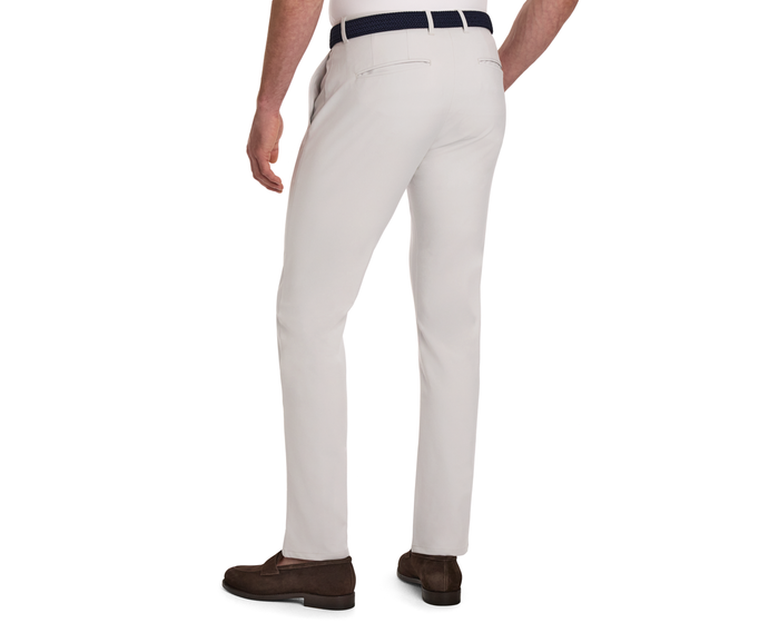 Rear view of The Anson Chino Pant: Stone, showcasing slim-fit design, classic slant pockets, dark belt, and brown suede loafers against a white background.