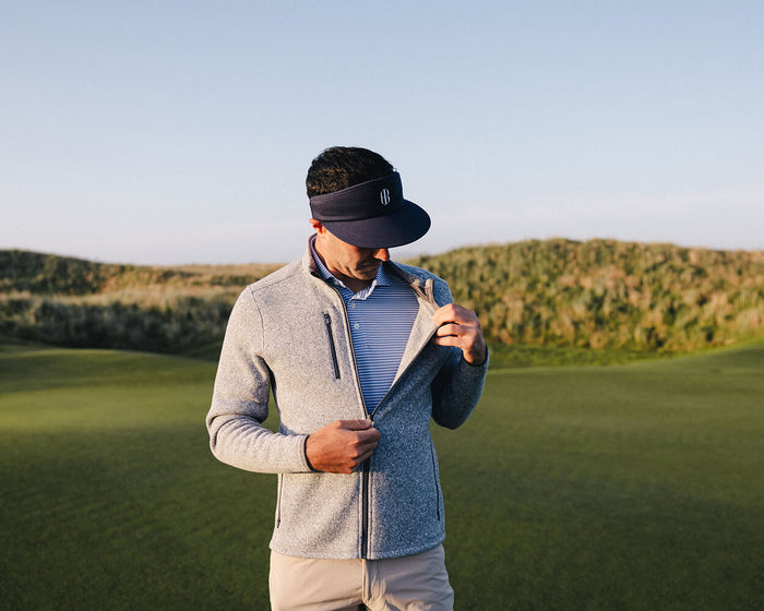 Man on a lawn adjusts The Ashby Jacket: Heathered Gray, showcasing its versatile midweight design with a brushed interior and stylish tonal accents.