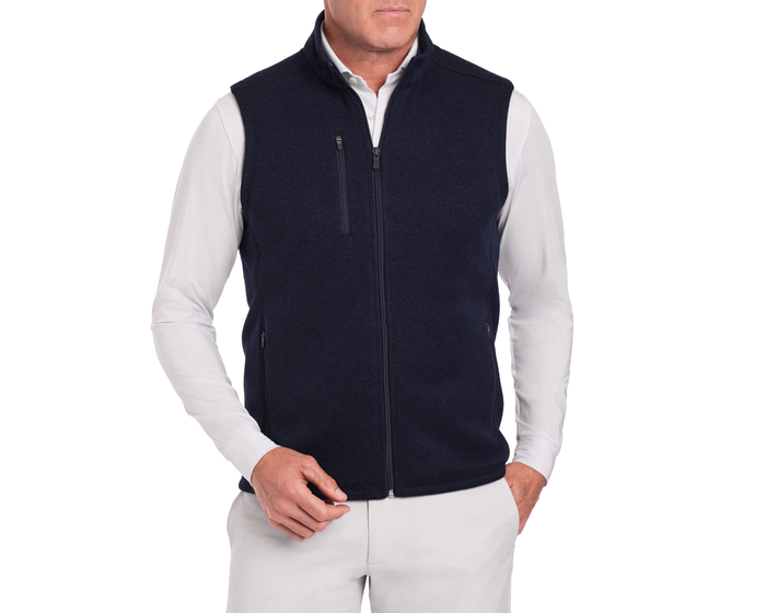 The Ashby Vest: Heathered Dark Navy, featuring a zip-front, stand-up collar, and low-profile pockets, worn over a white long-sleeve shirt.