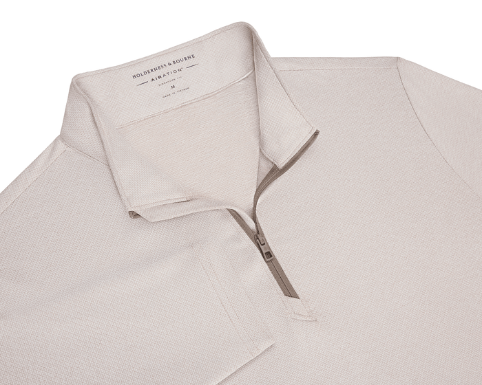 The Bell Quarter-Zip: Heathered Dune features a light-beige, quarter-zip design with a folded collar, textured knit, and modern drop-tail silhouette.