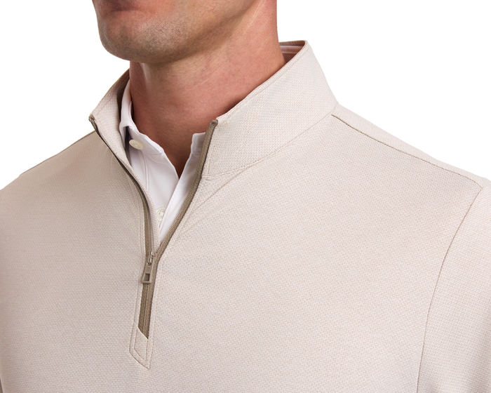 The Bell Quarter-Zip: Heathered Dune, showcasing a light-beige pullover with a textured collar and zipper, layered over a white button-down shirt.