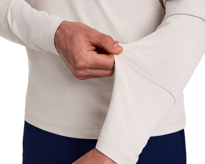 Person wearing The Bell Quarter-Zip: Heathered Dune, showcasing its textured fabric and modern silhouette, gently adjusting the sleeve for a sporty, sophisticated look.
