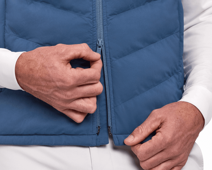 A person zips The Benton Vest: Andover, showcasing its quilted, sleeveless design with Thermore®-insulated front and knit back for comfort and mobility.