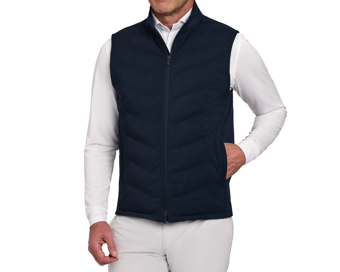 Person wearing The Benton Vest: Navy, featuring quilted design, sleeveless style, and high collar, with one hand in side pocket over a white shirt.