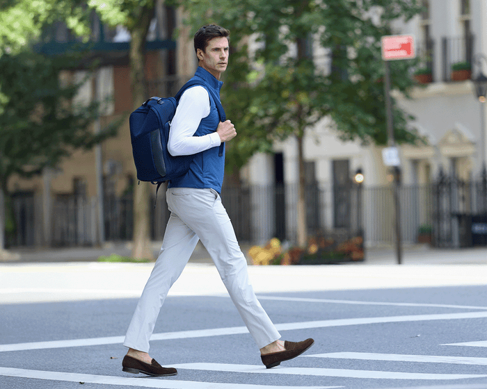 Man wearing The Broughton Backpack: Navy Ballistic - Navy Embroidery, smart-casual outfit, walking in urban street, showcasing the backpack's stylish, durable design.
