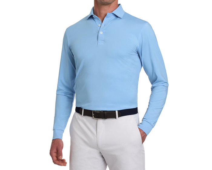 Model wearing The Farrell Shirt: Vista Blue, featuring long sleeves, a classic polo collar, and three-button placket, tucked into white trousers with a dark woven belt.