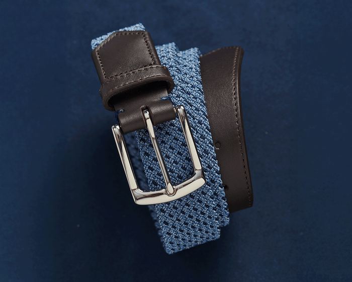 The Fischer Belt: Slate & Navy Basketweave features a light-blue woven strap, dark brown leather trim, and a polished silver buckle.