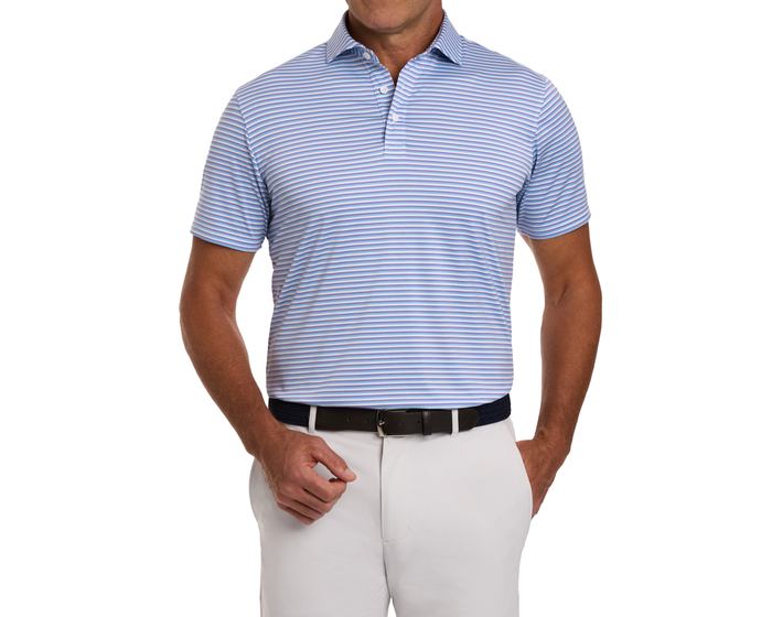 The Fleming Shirt: Tudor/Vista Blue/White, a light-blue and white striped polo, tucked into white trousers with a dark braided belt, offers comfort and sun protection.