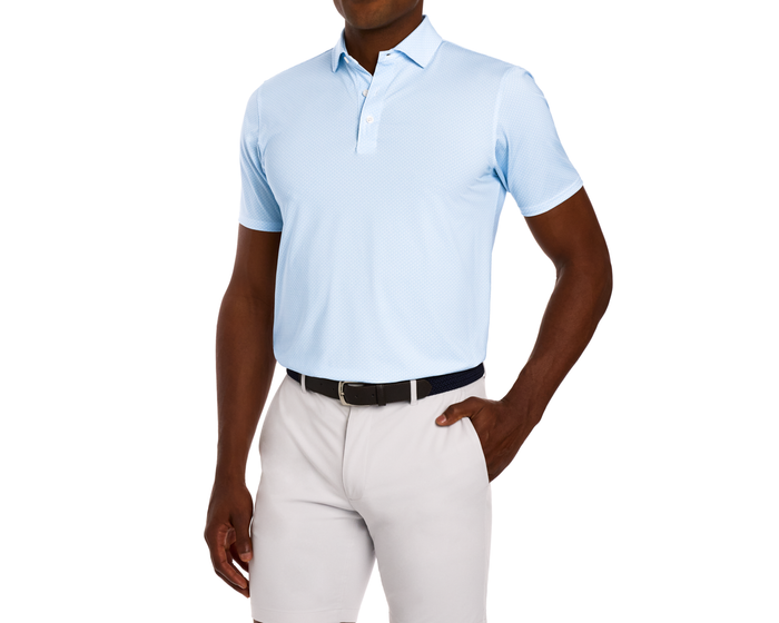 Model wearing The Hanover Shirt: Vista Blue, a light-blue polo with a geometric pattern, tucked into trousers, featuring a dark belt and structured collar.