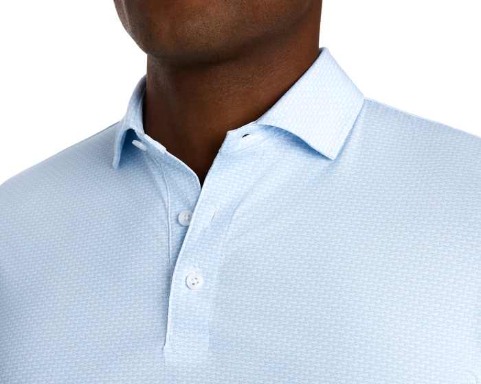 The Hanover Shirt: Vista Blue, featuring a light-blue polo design with a fine geometric pattern, white buttons, and a structured spread collar, offering comfort and breathability.