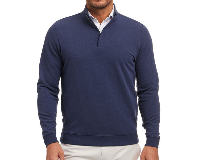 Man wearing The Harper Quarter-Zip: Heathered Atlantic, a navy pullover with a stand-up collar over a white shirt, paired with light-colored pants.