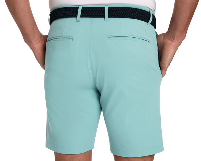 Lower back view of The Harwood Short: Cascade Green, featuring back welt pockets, braided belt, and hands in side pockets, highlighting comfort and performance details.