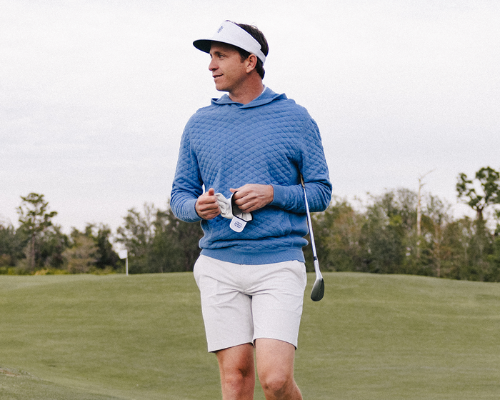 Man walking on golf course in The Harwood Short: Stone, featuring a non-slip waistband and ball-marker pocket, holding a golf club and glove.