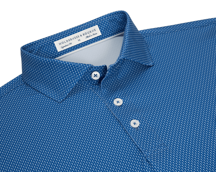 The Hicks Shirt: Maidstone Blue features a geometric golf-tee pattern, white dash motif, white buttons, and a structured collar, emphasizing performance and style.