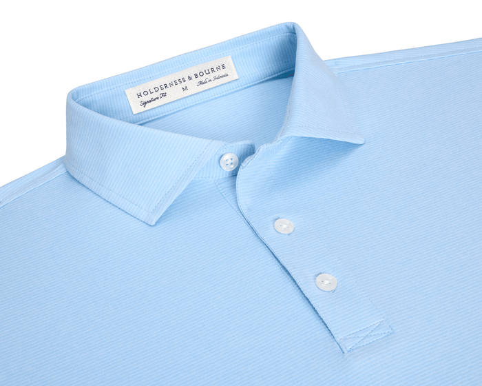 The Holland Shirt: Heathered Vista Blue, light-blue short-sleeve polo with a structured spread collar, subtle stripes, and three-button placket, displayed flat with visible label details.