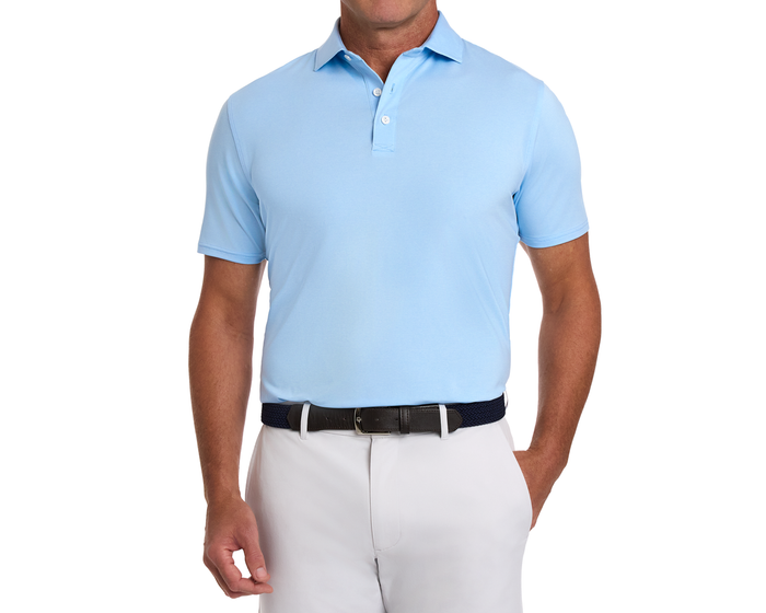 Man wearing The Holland Shirt: Heathered Vista Blue, showcasing a light-blue polo with subtle stripes, tucked into light trousers with a dark woven belt.