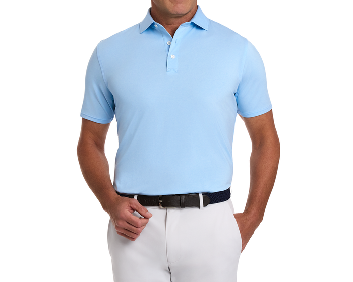 Man wearing The Holland Shirt: Heathered Vista Blue, a light-blue polo with subtle stripes, tucked into light trousers, accessorized with a dark woven belt.