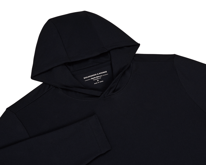 The Jackson Hoodie: Black, a sleek, lightweight pullover with no drawstrings or pouches, ideal for golf, displayed flat with visible Holderness & Bourne label.