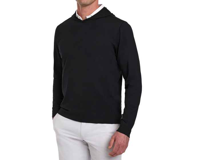 Male model wearing The Jackson Hoodie: Black over a white shirt, paired with light trousers, showcasing its streamlined design and soft performance fabric.