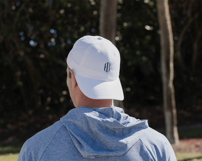 The Lightweight Performance Hat: White with HB Icon, worn backwards, shown on a person outdoors, features a streamlined design and adjustable closure.