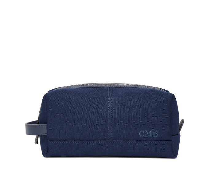 The Littler Dopp Kit: Navy Ballistic - Navy Embroidery, a sleek navy travel toiletry bag with a leather handle, top zipper, and debossed CMB initials.