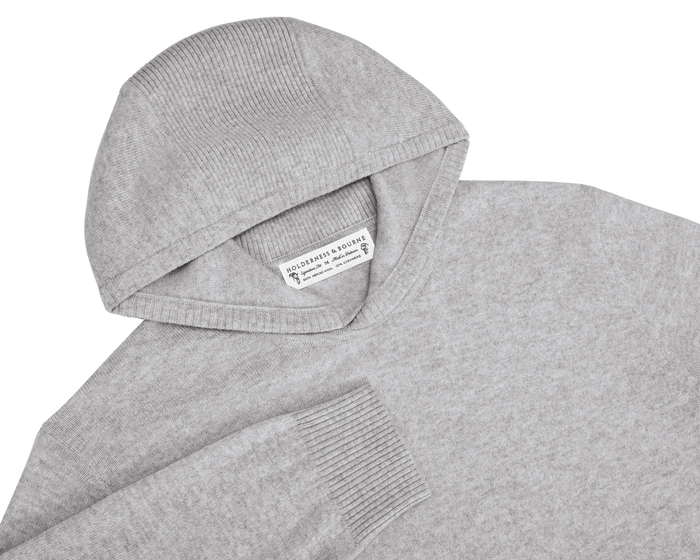 The Logan Hoodie Sweater: Heathered Gray, featuring ribbed detailing on hood and cuffs, crafted from soft Merino wool and cashmere, laid flat with visible label.