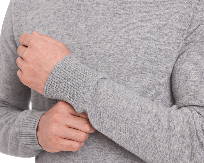 Person wearing The Logan Hoodie Sweater: Heathered Gray, adjusting ribbed cuff, showcasing its luxurious Merino wool-cashmere blend and minimalist design.