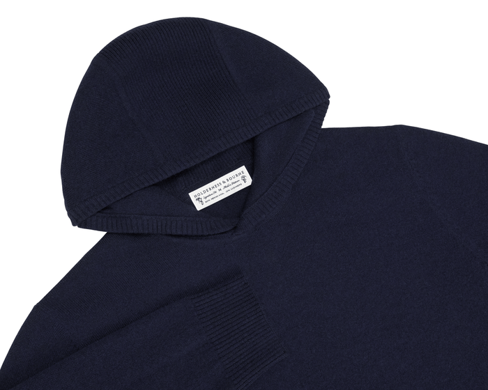 The Logan Hoodie Sweater: Heathered Navy, a navy-blue, hooded knit pullover featuring ribbed cuffs, a woven back label, and a minimalist design from Holderness & Bourne.
