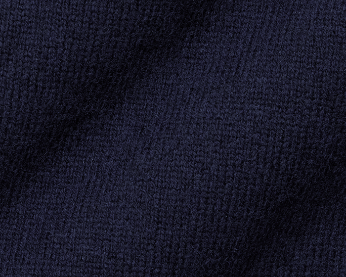 The Logan Hoodie Sweater: Heathered Navy, featuring a close-up of soft, dark-navy knit fabric with visible stitches, showcasing its luxurious Merino wool-cashmere blend.