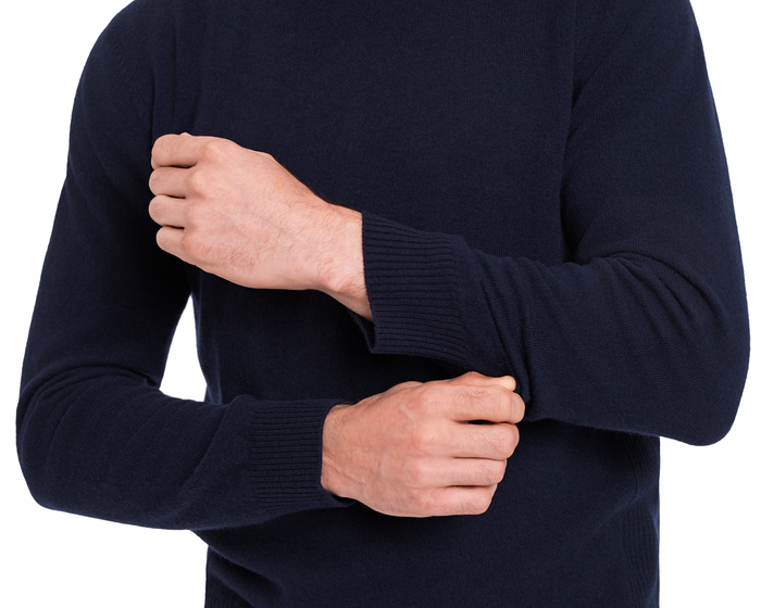Person adjusting sleeve of The Logan Hoodie Sweater: Heathered Navy, showcasing its luxurious Merino wool and cashmere knit with ribbed cuff detailing.